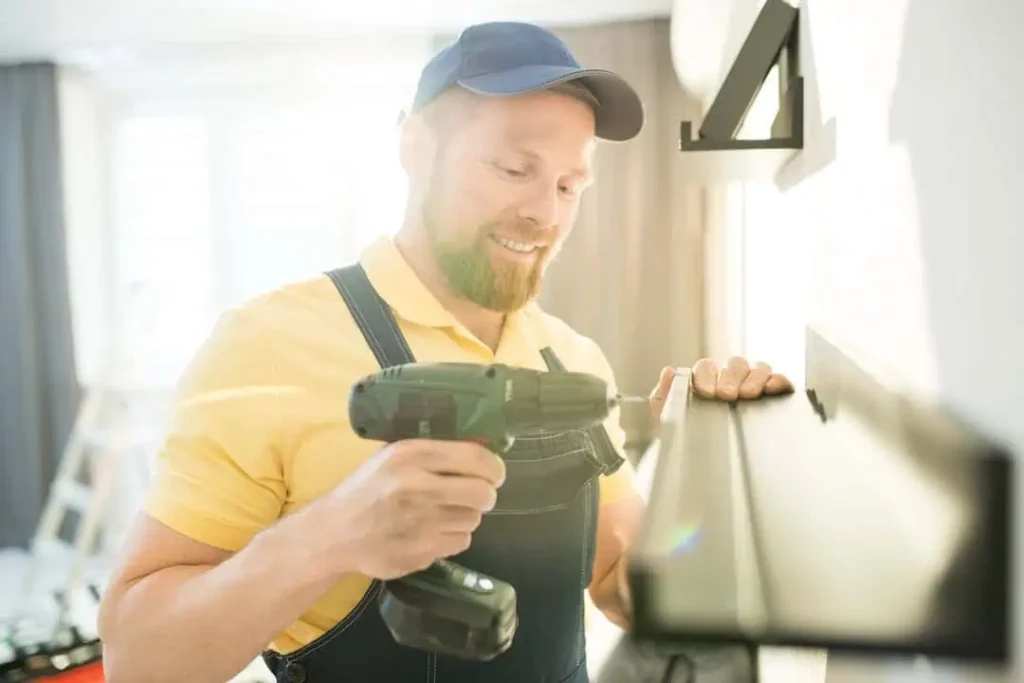 A handyman with a drill in hand installing a shelf