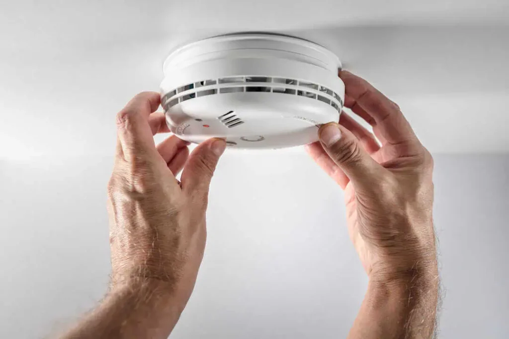 a smoke detector with two hands touching it