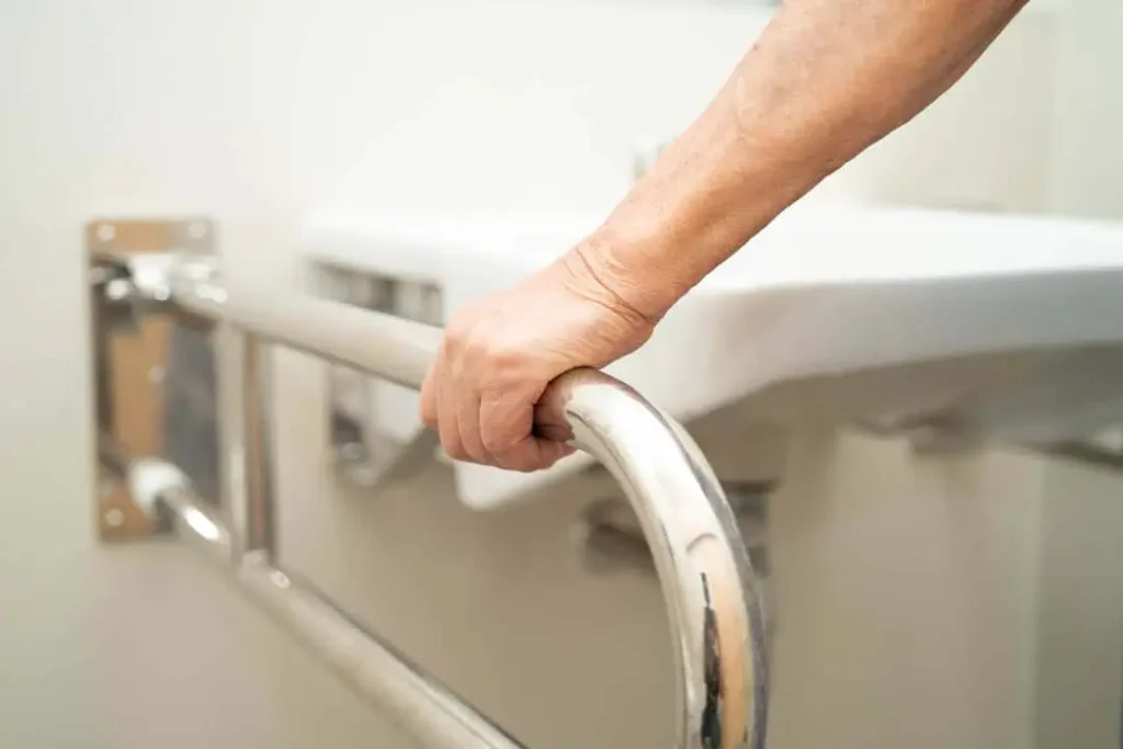 a grab bar next to a sink in a bathroom with a hand holding onto it